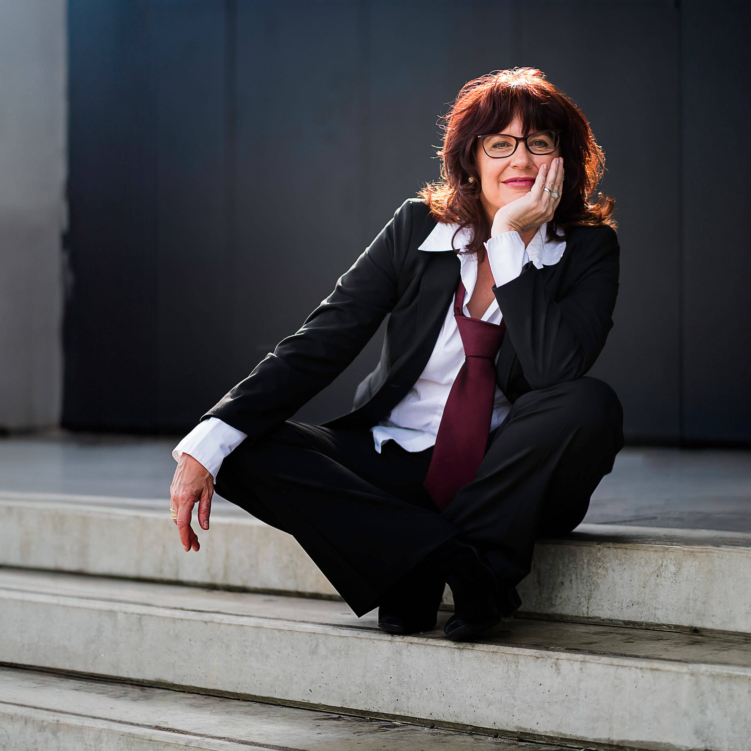 Sibylle Teschner sitzt entspannt und selbstbewusst auf einer Treppe.